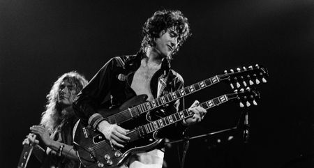Jimmy Page plays his double-neck onstage with Led Zeppelin as frontman Robert Plant plays the tambourine in the background. 