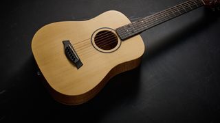 A Taylor BT1e Baby Taylor 3/4 acoustic guitar on a black floor