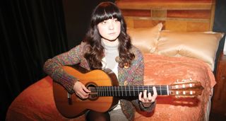 Classical phenom Laura Snowden sits on a bed and plays her custom made Christopher Dean guitar